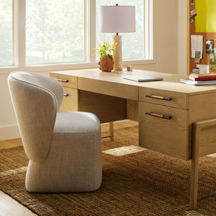 Wooden desk with a lamp, chair, and accessories in a home office setting.