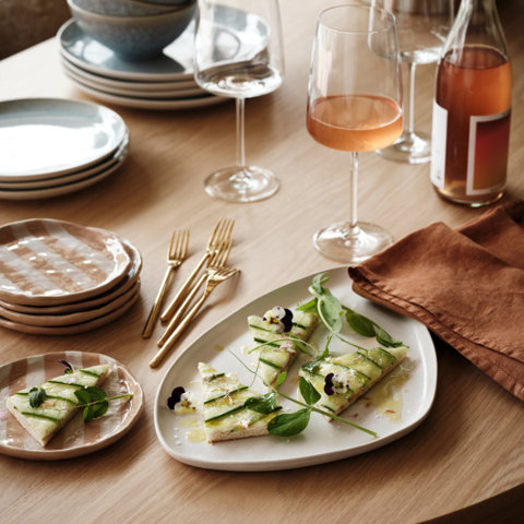 Table setting featuring white and pink plates, gold forks, wine glasses, and food.