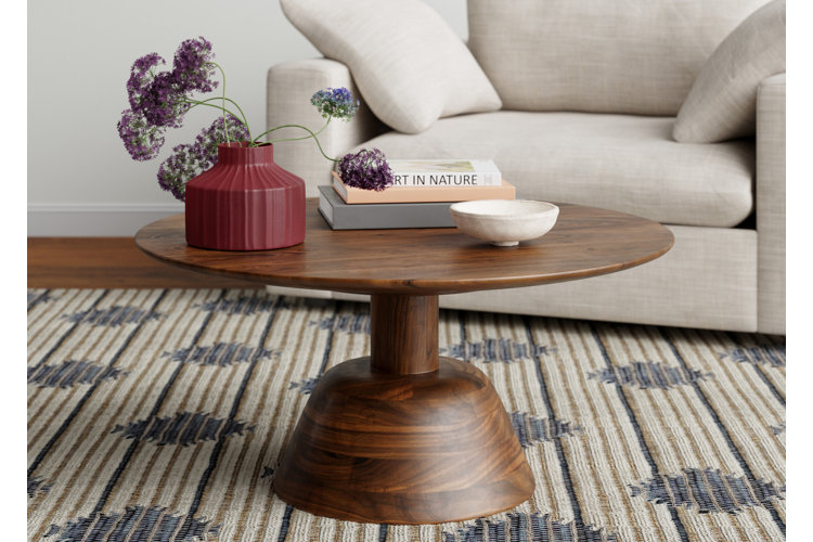 wood pedestal coffee table with a dark red vase, stack of books, and a small white bowl