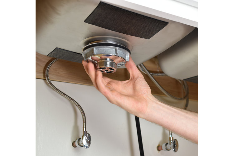 A person's hand removing the housing unit from a kitchen drain underneath a sink.