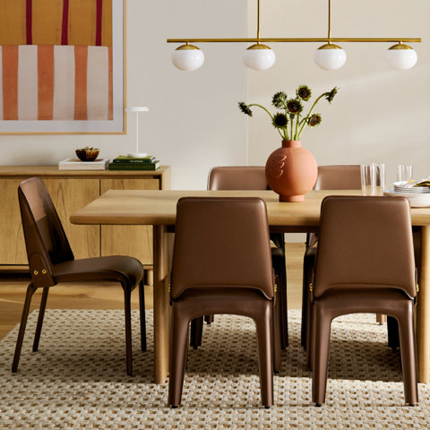 Round wooden dining table with chairs in a bright dining room.