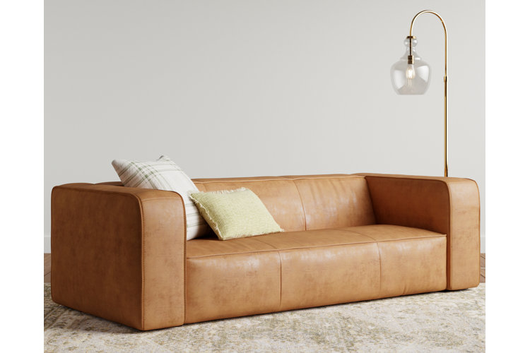 warm brown leather match sofa with two throw pillows and a gold floor lamp