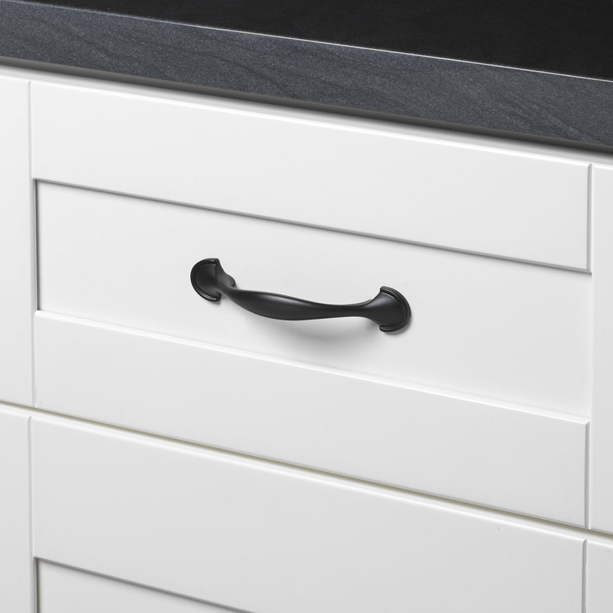 Matte black drawer pull hardware installed on a white shaker-style cabinet drawer with a black countertop.