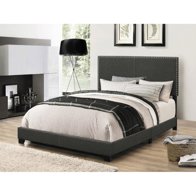 Très grand lit à panneau tapissier gris anthracite avec quatre pieds de soutien, garniture cloutée classique et conception rectangulaire pour une chambre de couleur, de style et de pieds décoratifs