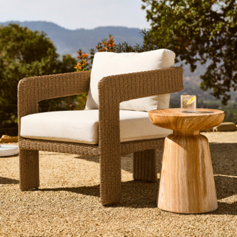 Wicker chair with cream cushions next to a wooden side table.