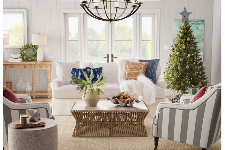 Coastal living room with a green Christmas tree in the corner, a white slipcover sofa, and a white and gray stripe chair.