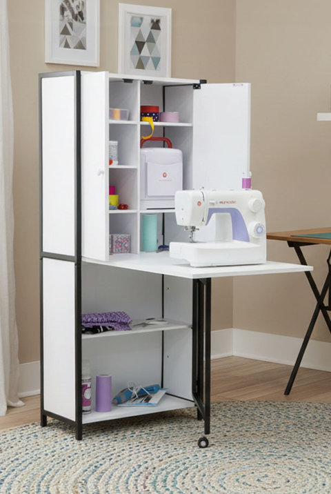White sewing cabinet with open shelves, a fold-out workspace, and a sewing machine on a light wood floor.