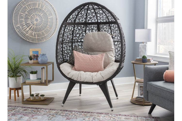black rattan balloon chair with a pink throw pillow in boho living room in front of a circular tan rattan wall hanging