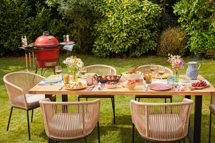 red BBQ behind a wood outdoor dining table