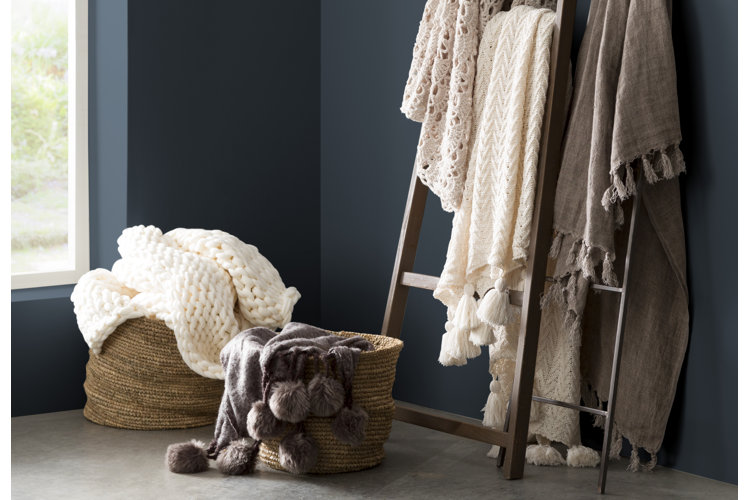 Blanket display with throw blankets in wicker baskets and three blankets draped over two blanket ladders
