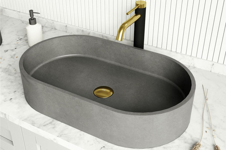 modern oval vessel bathroom sink in matte gray with a gold drain cover and matching gold faucet on a white marble countertop