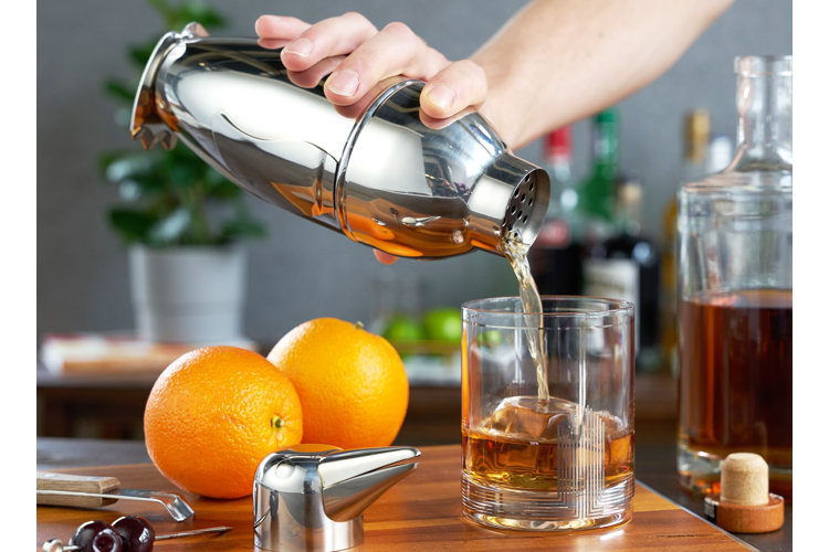 What is a cocktail shaker hand pouring a cocktail from a silver cocktail shaker into a clear glass cocktail glass