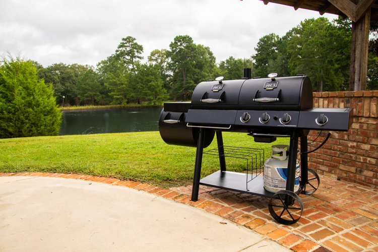 an offset smoker set up in a back yard on a brick patio