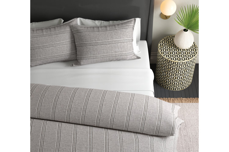 Close up of a black bed with white sheets and gray striped bedding and bed pillows.