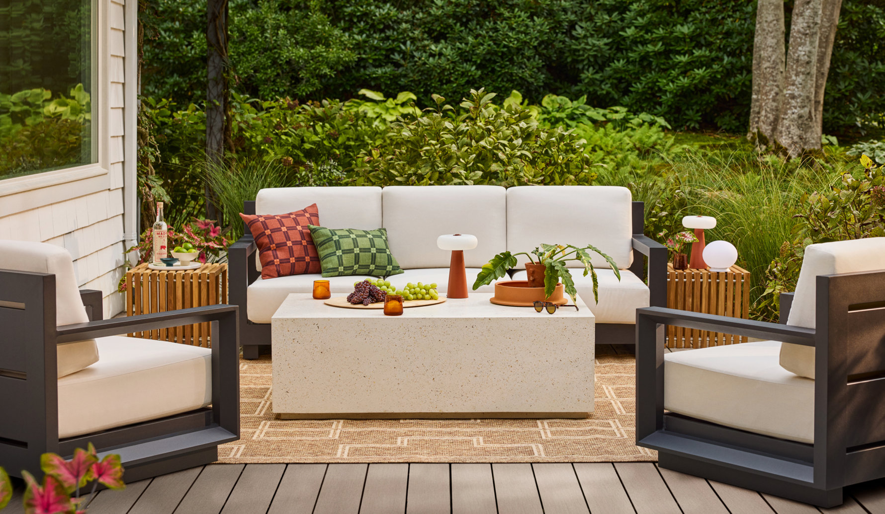 Modern outdoor seating set with a white sofa, two armchairs, and a speckled stone coffee table arranged on a patterned rug on a patio.