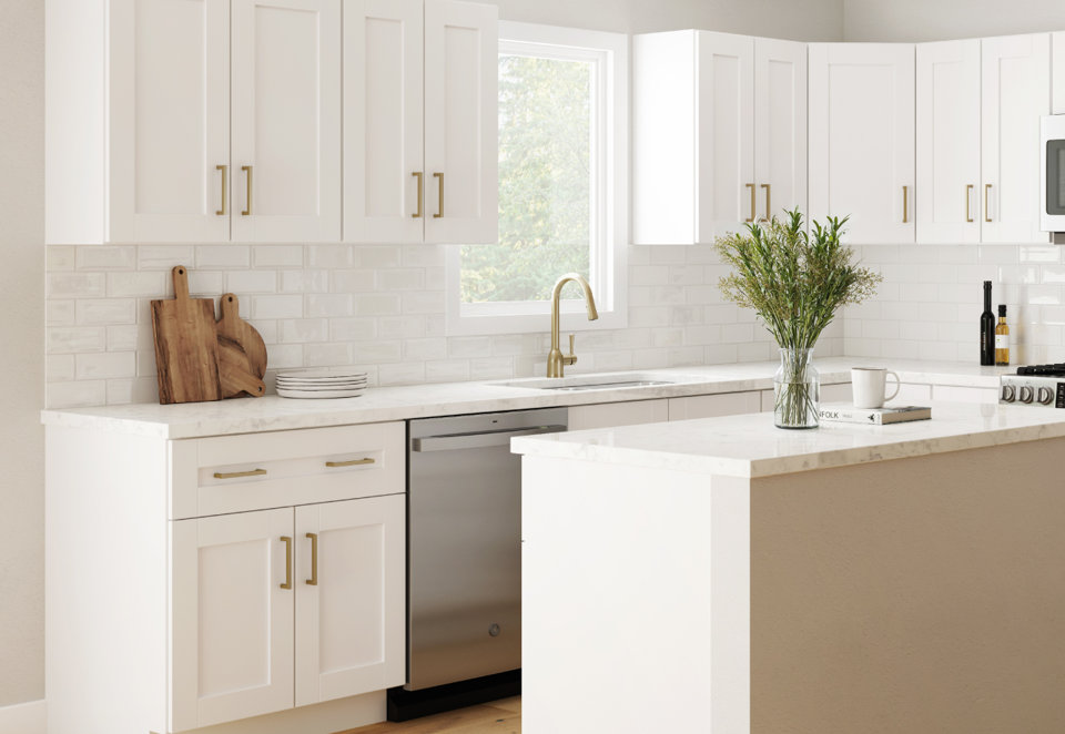 Bright white shaker cabinets with gold hardware and a marble countertop in a modern kitchen with a stainless steel dishwasher.