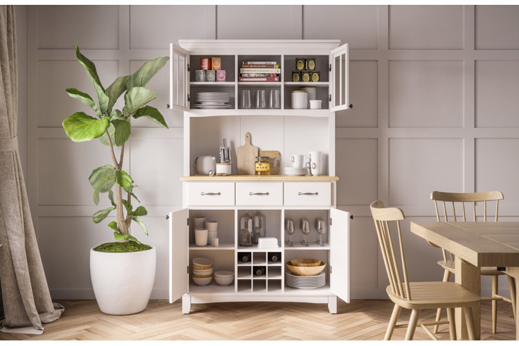 white kitchen hutch with open shelves, drawers, and cabinets displaying dishes, glassware, and decor beside dining table and potted plant