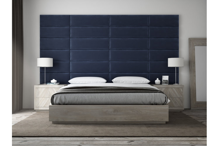 Modern bedroom with a low-profile headboard-free bed frame up against a wall with navy blue upholstered paneling.