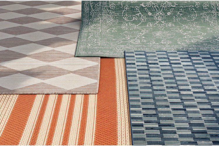 four patio rugs: neutral diamond-patterned outdoor rug, orange striped patio rug, green floral area rug, and a blue geometric patio rug