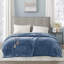 Sapphire blue heated plush electric blanket with two controllers draped over a bed with a gray tufted headboard.