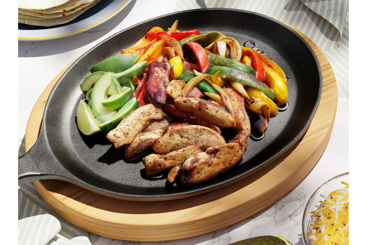 Close up of a an oval-shaped cast iron frying pan with limes, grilled chicken strips, and sliced peppers for fajitas.