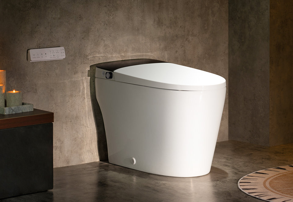 Modern white smart toilet with a sleek black lid mounted in a contemporary bathroom with stone-textured walls and ambient candle lighting.