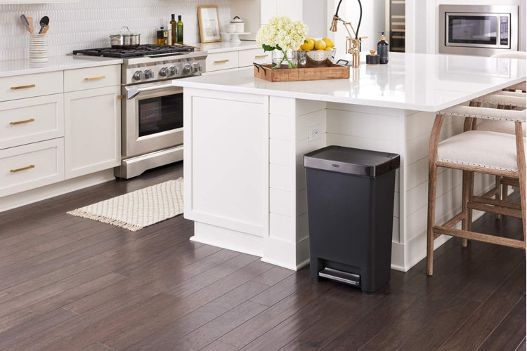 a black step-on trash can tucked beside a white marble kitchen island