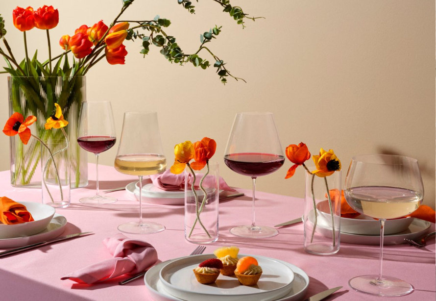 A table setting with red and white wine glasses, tulips, dessert pastries, plates, and silverware.