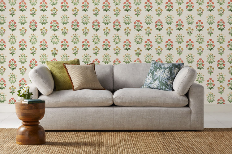 what is a loveseat gray loveseat with two cushions and three multicolored and patterned throw pillows, patterned wallpaper behind and a neutral beige area rug and wooden side table
