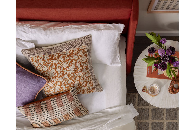 red upholstered bed topped with white sheets, orange pillows, and one purple throw pillows