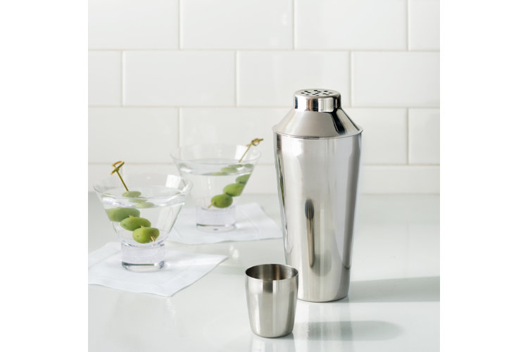 stainless steel cocktail shaker pictured next to two martinis with olives