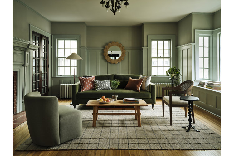 A living room with green color drenched walls a green velvet sofa, a green accent chair and a light wood coffee table