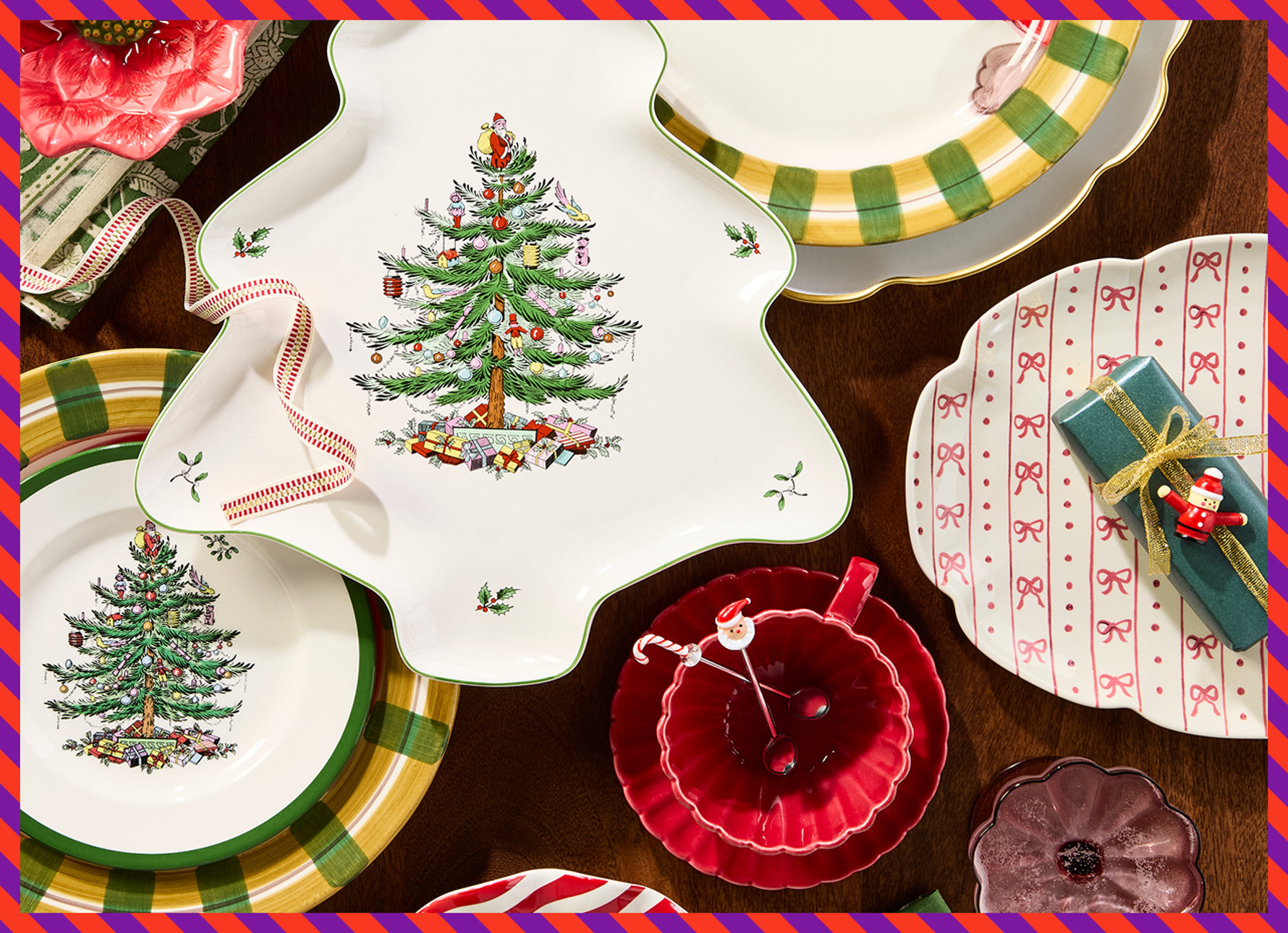 Top-down view of Christmas dinnerware featuring a tree-shaped platter, plates with festive tree and ribbon patterns, a red bowl with Santa spoons, and wrapped gifts on a wooden table.