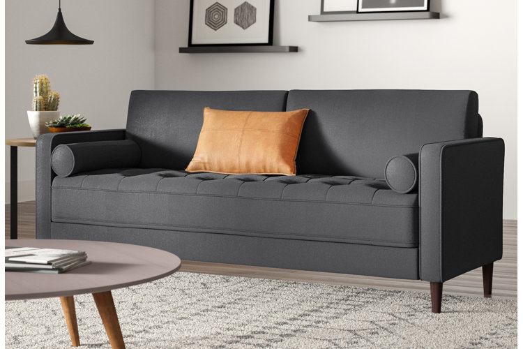 a gray tufted sofa with a leather accent pillow