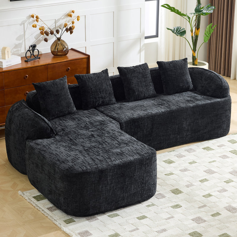 Canapé de coin comprimé en chenille noire, garni de mousse souple haute élasticité, incurvé et doté de quatre coussins décoratifs. Parfait pour le salon et la chambre. Assise mi-ferme, support par ressorts.