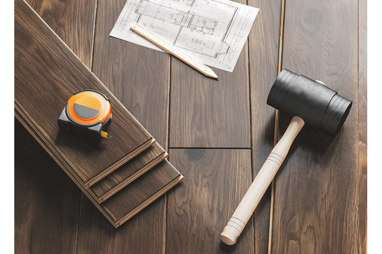 flooring planks, blueprints, mallet, measuring tape, and carpenter's pencil on a wood floor