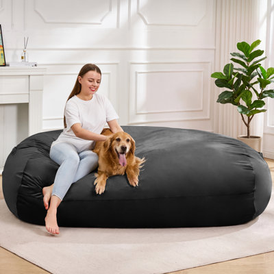 Pouf géant de 1,80 m en velours noir, sans os et en mousse mémoire compressée. Housse amovible et poche latérale pour salon ou chambre.