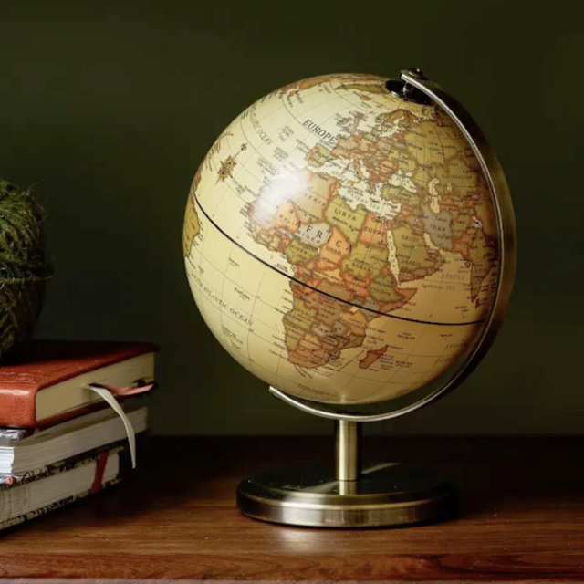 Vintage-style world globe on a bronze stand resting on a wooden desk beside a stack of books.