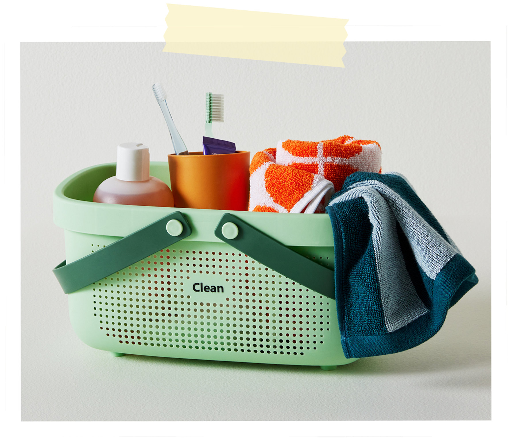 A mint green plastic bath caddy labeled Clean, filled with toiletries, toothbrushes, and folded towels.