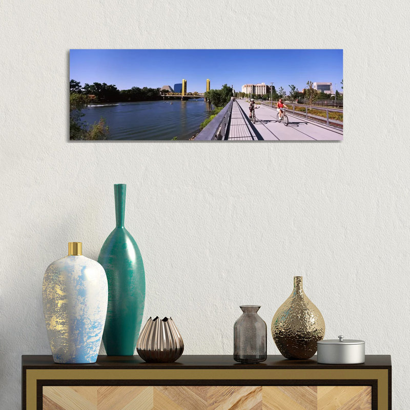 Bicyclists Along The Sacramento River With Tower Bridge In Background, Sacramento, Sacramento County, California, USA by Panoramic Images - Wrapped Canvas Panoramic Print