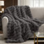 Dark gray faux fur throw blanket with a textured bubble wave design draped over a beige sofa.