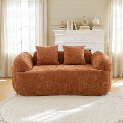 Orange Curved two - person compress  sofa. It has armrests on both sides, comes with two pillows, is  for small - sized apartments