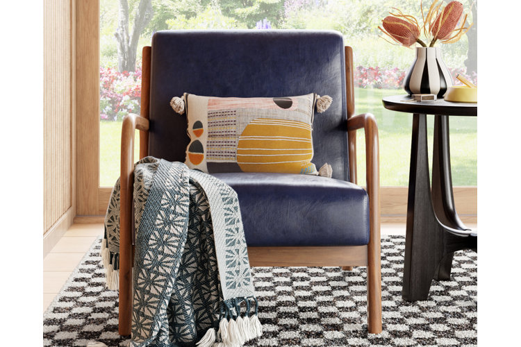 mid-century modern armchair with navy leather upholstery, topped with a boho throw blanket and throw pillow