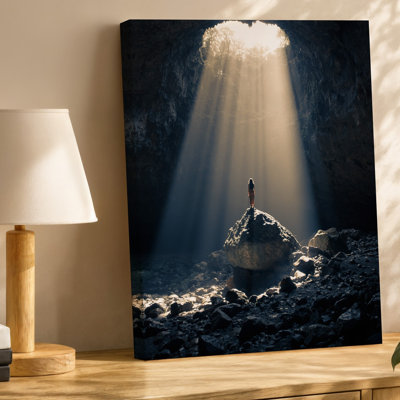 Toile, une figure solitaire se dresse sur une formation rocheuse à l'intérieur d'une vaste grotte sombre illuminée par des arbres dramatiques de lumière