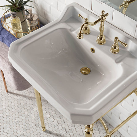 White porcelain sink with gold faucet and gold stand.