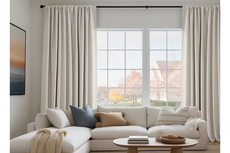 Living room with an ivory sectional up against an open window with ivory curtains hanged on either side of the window.