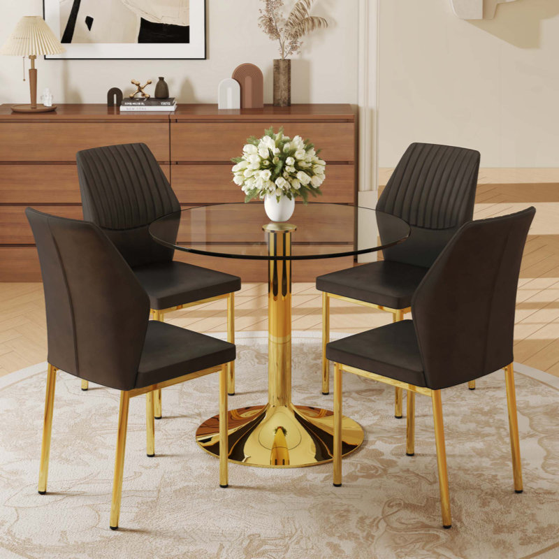 Une table de salle à manger ronde en verre trempé - support et base en métal, jumelé à 4 chaises de salle à manger en polyuréthane à haute résilience avec pieds en métal.