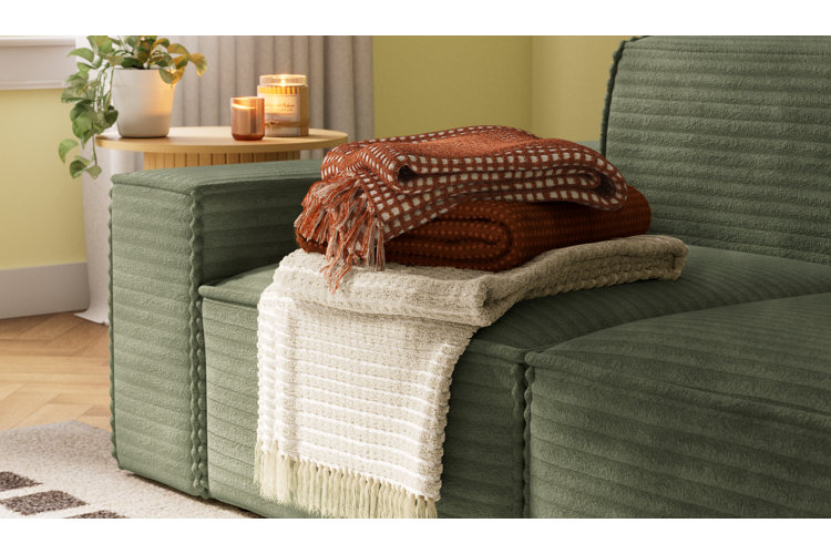 modern living room with green sofa, three folded throw blankets, wood side table, and two glowing candles