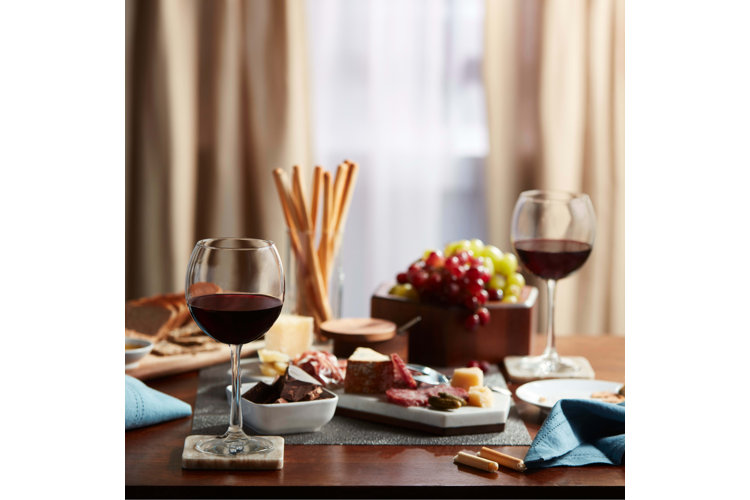 Dining table with two glasses of red wine, dark chocolate, grapes, cheese and meat spread, and bread sticks.