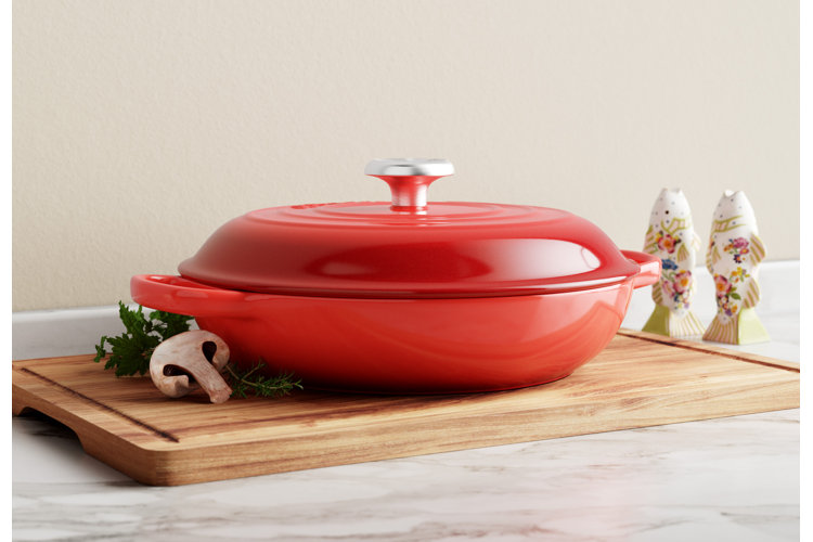 Red braiser next to a cutting board with lettuce.